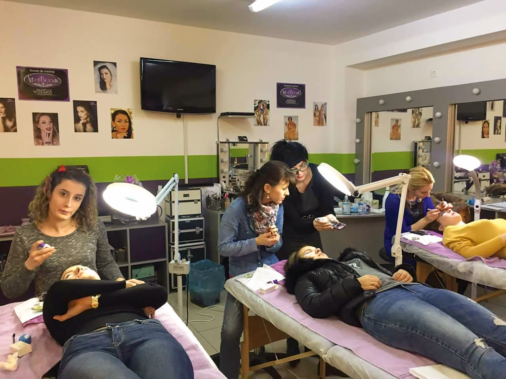 Nicoleta Streja, fondatoarea VogueLash Academy din Reading, Marea Britanie, îmbrăcată într-un sacou roșu și ținând pensule de machiaj în mână.